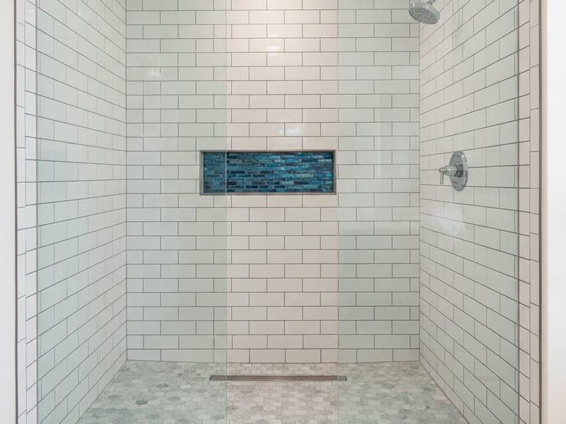 Tile setter installing large subway tile on a shower wall in a San Diego County bathroom with waterproofing membrane visible at the base
